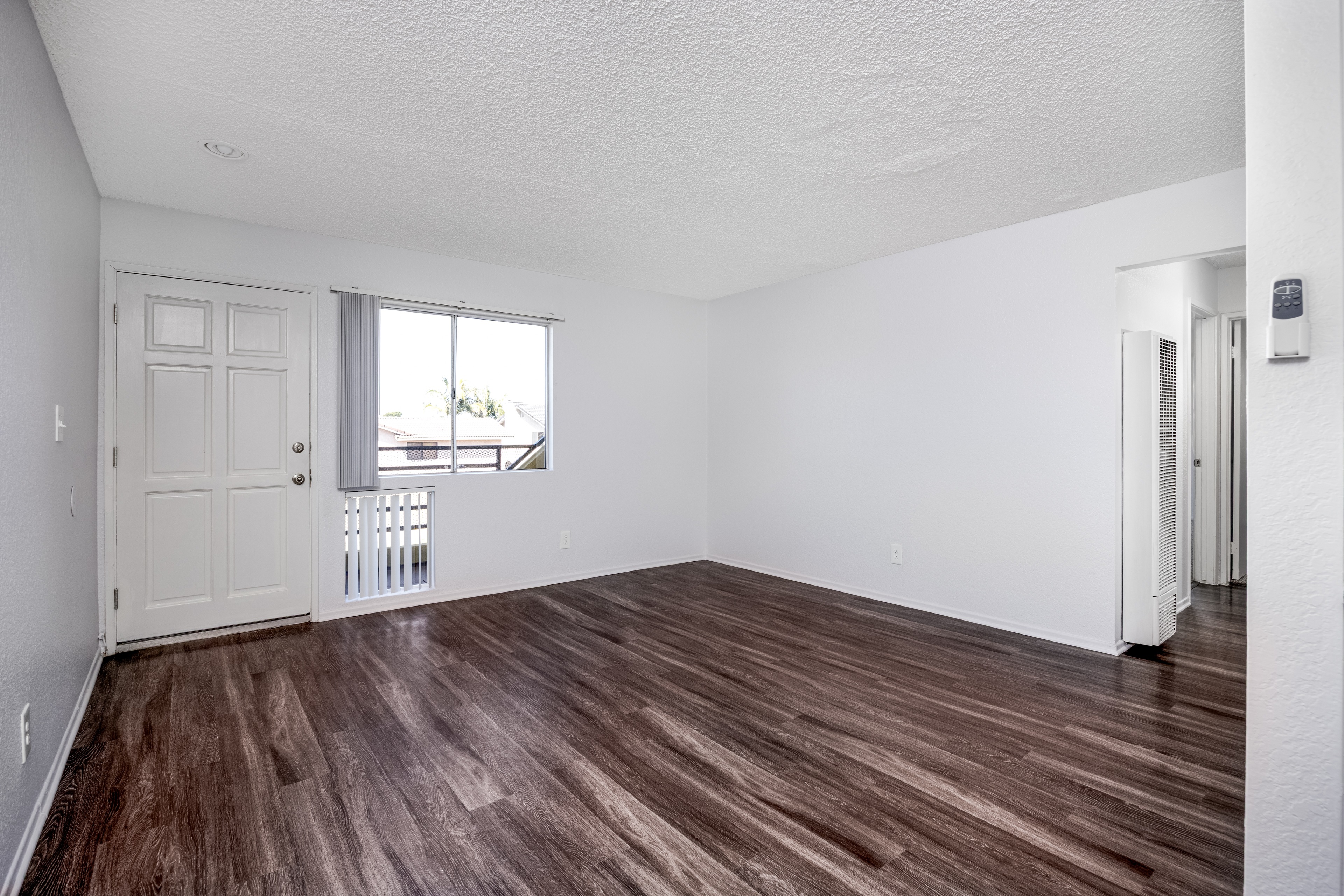 A room with a white door and a window with a view of a balcony.